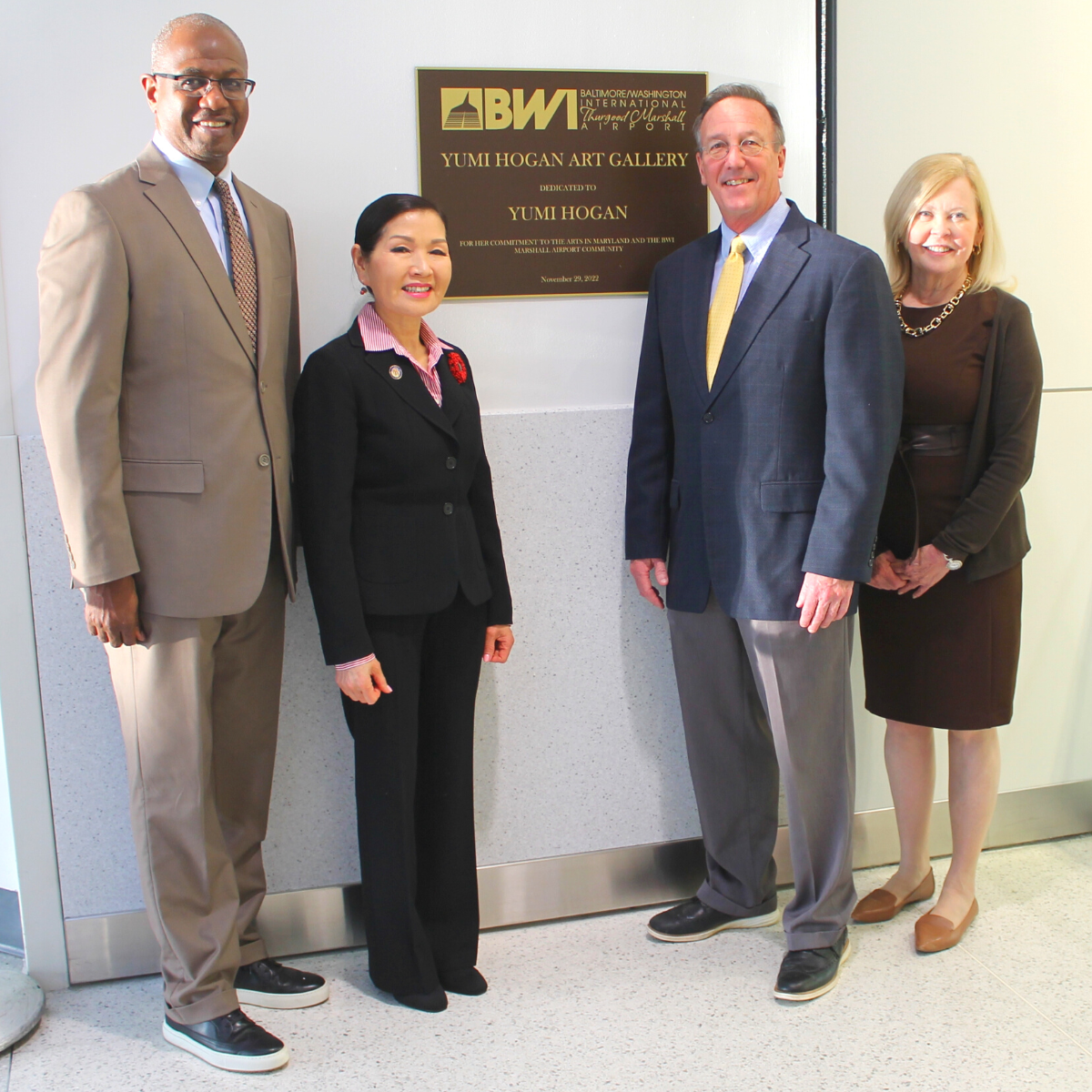 Photo of BWI Marshall Airport Executive Director Ricky Smith, Maryland First Lady Yumi Hogan, Maryland Department of Transportation Secretary Jim Ports and Arts Council of Anne Arundel County Executive Director April Nyman standing near a sign commemorating the renaming of the Yumi Hogan Art Gallery space at BWI Marshall Airport
