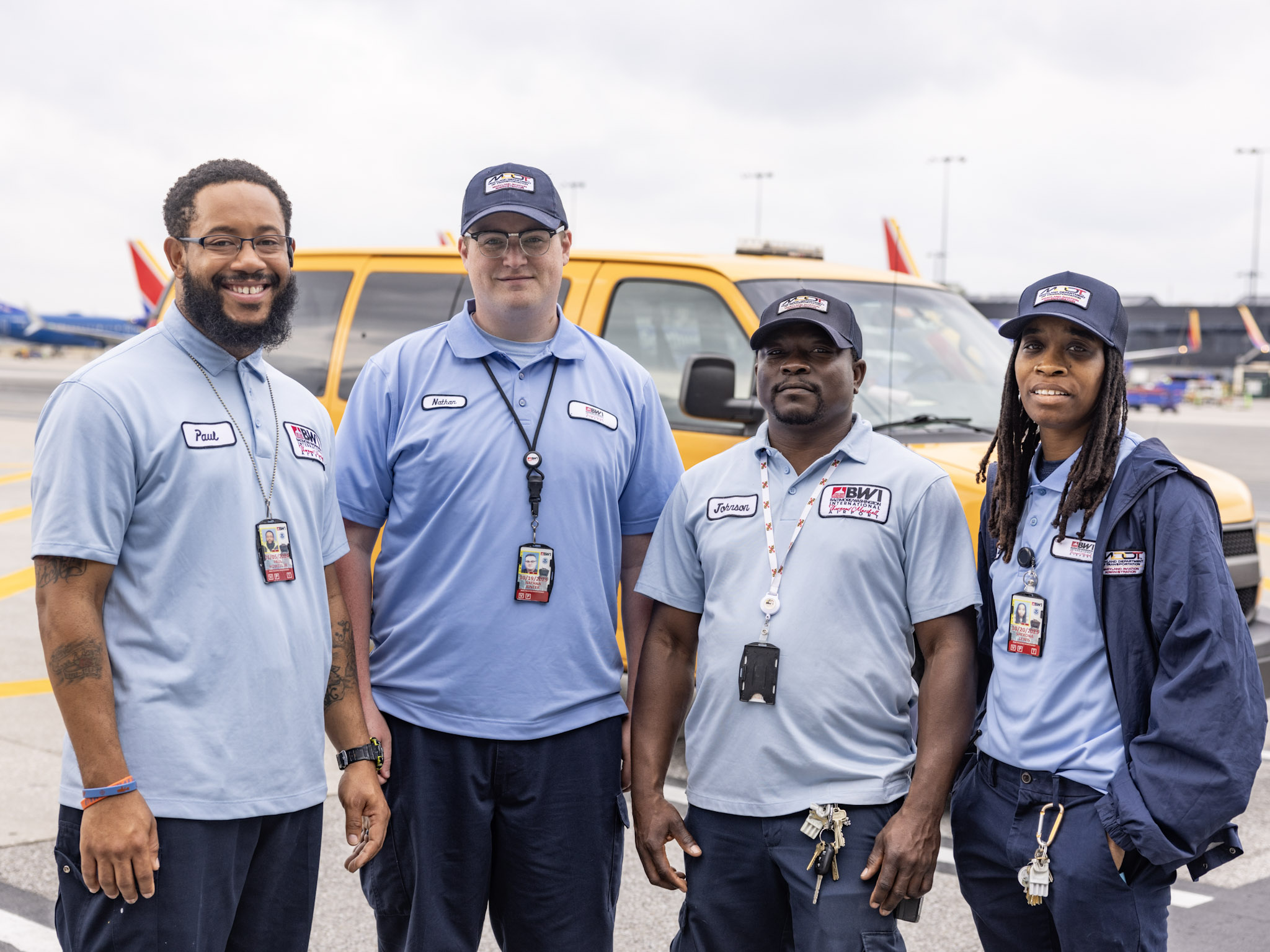 Photo of 4 members of the BWI Marshall Airport Operations and Maintenance team standing posing for a photo with an airport vehicle and aircraft in the background.