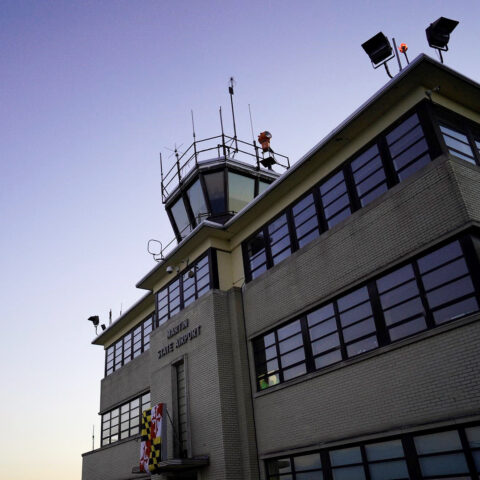 Square photo of the Martin State Airport terminal exterior with a purple dusk sky in the background.