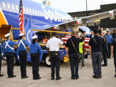Photo of individuals saluting as a flag-draped casket is unloaded from a Southwest Airlines aircraft during a dignified transfer at BWI Marshall Airport.