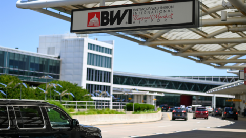 Photo of a BWI Marshall Airport logo sign along the airport's Departures Level roadway with vehicles in the background