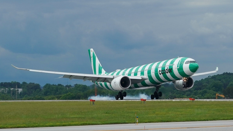 Photo of a Condor Airlines aircraft with green stripes and smoke trailing its tires upon touchdown at BWI Marshall Airport.