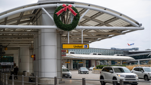 Photo of a wreath with holidays displayed near the top of the end on a terminal roadway canopy at BWI Marshall Airport with a departing Southwest Airlines aircraft in the background.