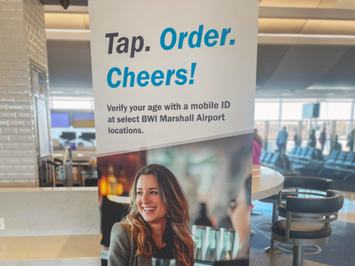 Photo of a pop-up banner near the bar of a restaurant at BWI Marshall Airport highlighting the use of Mobile ID for age verification at select airport restaurants.