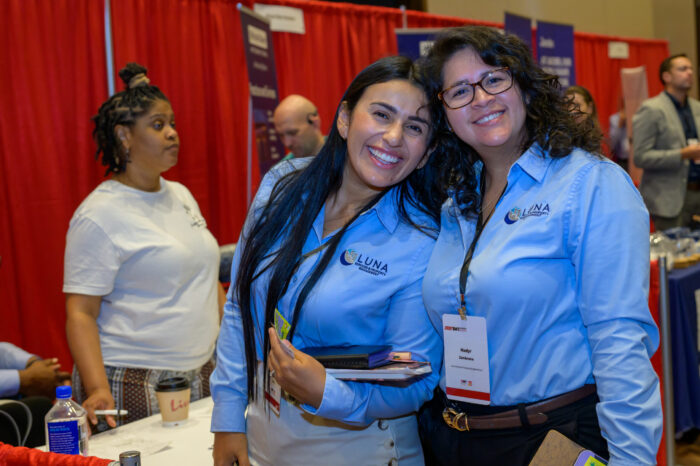 Two exhibitors pose for a photo near their booth in the exhibit hall of the 2025 SynergyBWI Business and Networking event.
