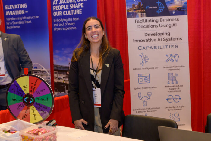 An exhibitor poses for a photo at their booth in the exhibit hall at the 2025 SynergyBWI Business and Networking event.