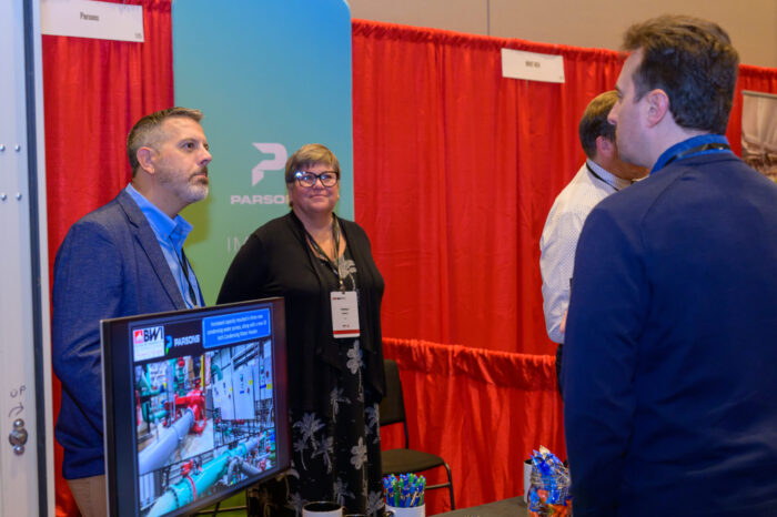 Photo of two exhibitors talking with a event attendee in the exhibit hall of the 2025 SynergyBWI Business and Networking event.