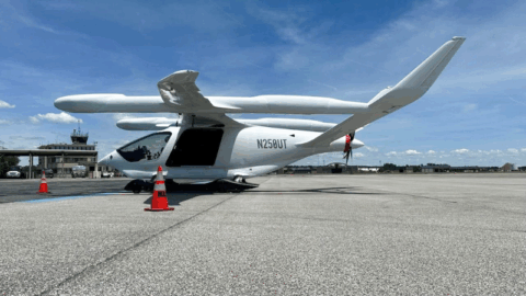Photo of an electric aircraft parked at Martin State Airport with the airport's terminal building in the distant background.