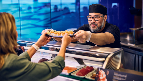 A restaurant worker hands a sushi plate to a passenger at a BWI Thurgood Marshall Airport restaurant.