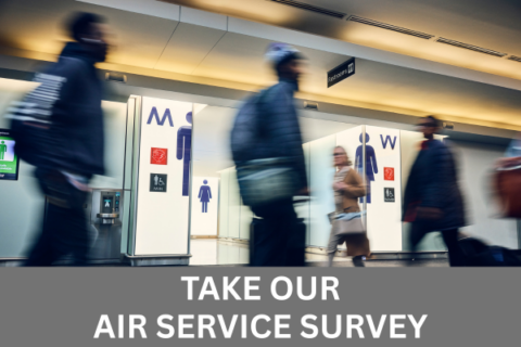 Long exposure photo of passengers walking by the entrance to renovated restrooms at BWI Thurgood Marshall Airport with white text in a grey box along the bottom of the image that reads Take Our Air Service Survey.